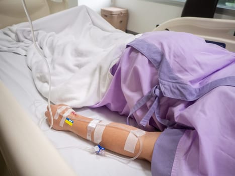 close up of saline solution on hand of women patient in pink clothes lying on the hospital bed