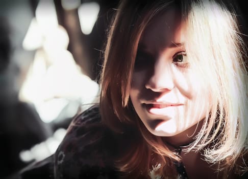 Bright sunlight through the window illuminated the smiling face of an attractive young blond woman. Portrait headshot with shallow depth of field, contrasting shadows, soft selective focus.