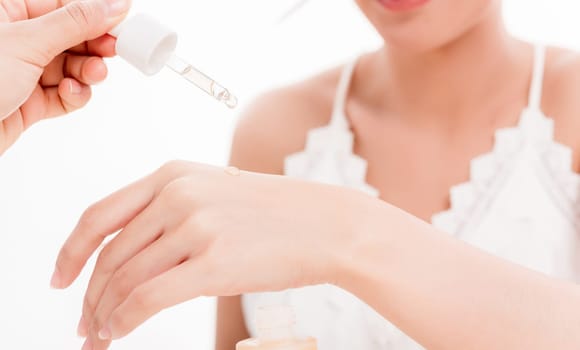 Beautiful woman dropping serum collagen moisturizer into back of the hand to present skin care product isolated on over white background, Vitamin C or E, Beauty and spa concept