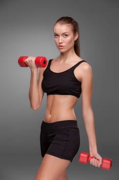 Sporty woman doing aerobic exercise with red dumbbells on grey background