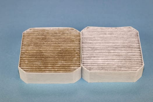 Two air filter on a blue background, one on the left is dirty and the one on the right is clean. One dirty and one clean square gray and white air filters next to each other on a light blue background
