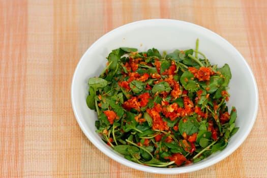 Watercress or cress with red bell pepper, carrot, ginger, lime juice, olive oil, salt and ground black peppercorn. Watercress and vegetable salad with homemade dressing in a round white bowl close-up
