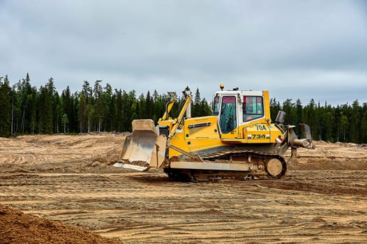 A yellow tractor bulldozer stands in a sand pit. High quality photo