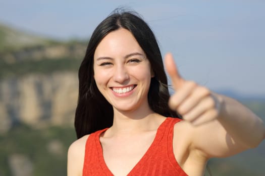 Front view portrait of a happy asian woman gesturing thumb up in the mountain