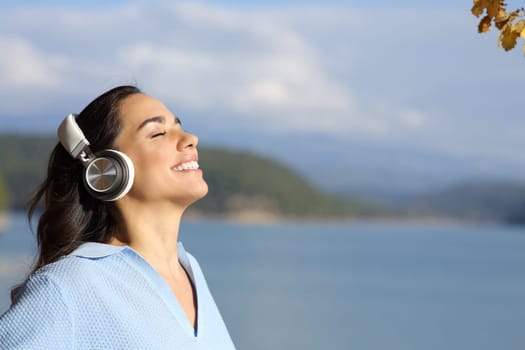 Happy woman meditating wearing wireless headphones in a lake