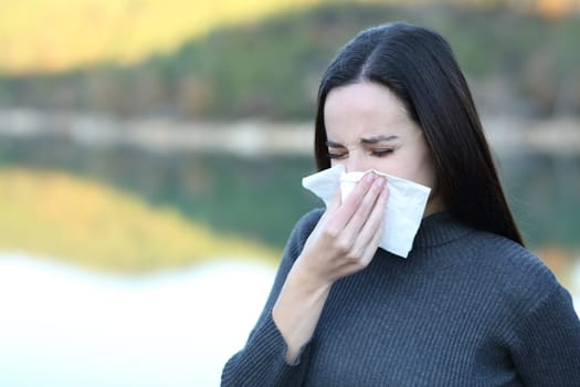 Ill woman blowing nose with a tissue outdoors in winter