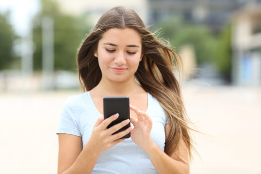 Front view portrait of a teenage walking using smart phone in the street