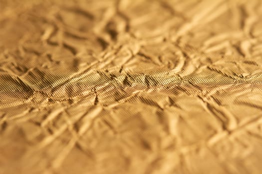 top view detail closeup of textured wrapping paper gold foil leaf with wrinkled surface and shallow depth of field