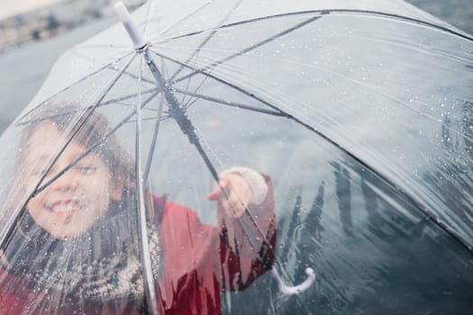 front view closeup portrait of happy little girl dressed in red and holding a transparent umbrella with rain drops