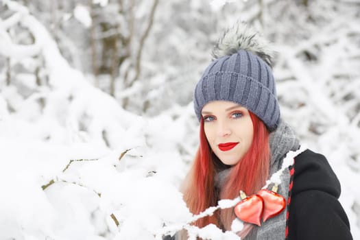 Attractive red hair girl is posing with  with two connected red hearts in the snowy nature.