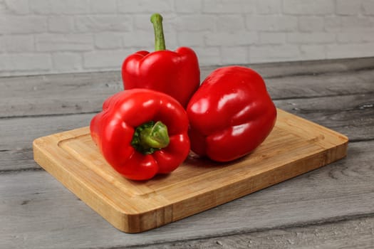 Three whole red bell peppers on chopping board
