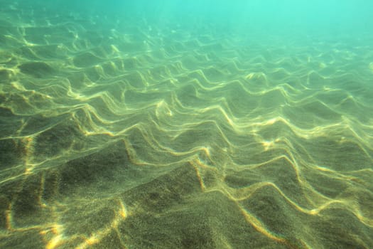 Sea bottom, sand "dunes"" lit by sun, turquoise water in distance. Underwater photo - abstract marine background"