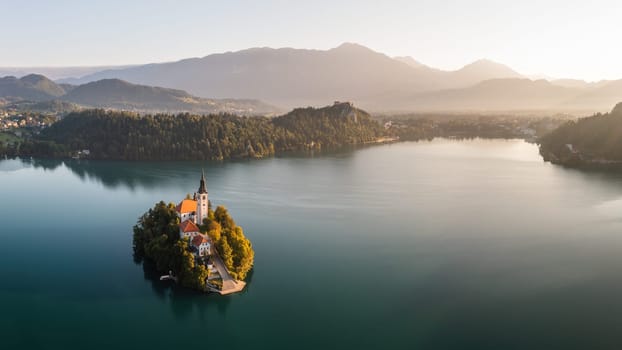 Historical castle on island in tle middle on Bled lake. Panoramic view on tourist destination in Slovenia Julian alps. Famous building in morning sunrise.