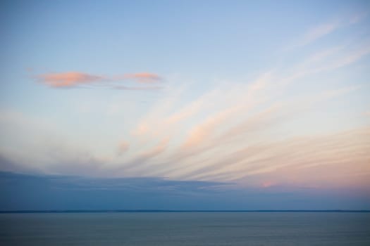 Tranquil nature scenery with long clouds covering blue sky after sunset. Peaceful wide angle view of a still water in summer. Horizontal seascape with copy space