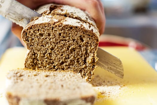 Slicing fresh rye bread with a big knife in a a domestic kitchen. Healthy food and source of fiber. Bakery product