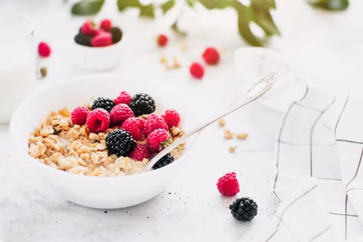 Morning healthy breakfast, white bowl full with granola, muesli, raspberry, blackberry on gray concrete table. Healthy eating, eco, bio food concept. Fresh tasty meal on grey background. Quality photo