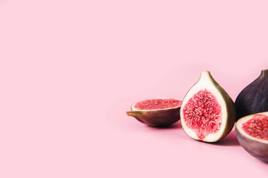 Fresh tasty fig fruit halves with shadow on pink background table with empty copy space. Many cross sections of fig tree fruit. Vegan desert concept. Shadow of healthy eating food. High quality photo