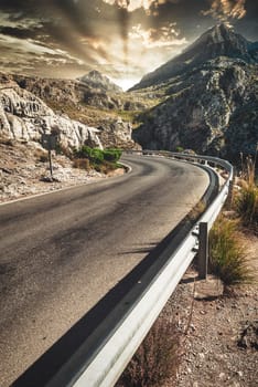 Serpentine road Street serra tramuntana, Majorca during sunset with sunlight and mountain peak in background