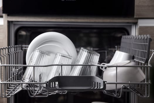 Front view of open automatic stainless fully integrated dishwasher range machine with clean utensils, cutlery, inside at modern home kitchen. Household domestic, kitchen appliances, lifestyle view