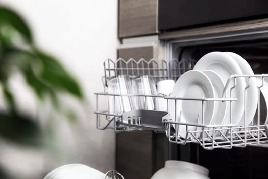 Front view of open automatic stainless fully integrated dishwasher range machine with clean utensils, cutlery, inside at modern home kitchen. Household domestic, kitchen appliances, lifestyle view