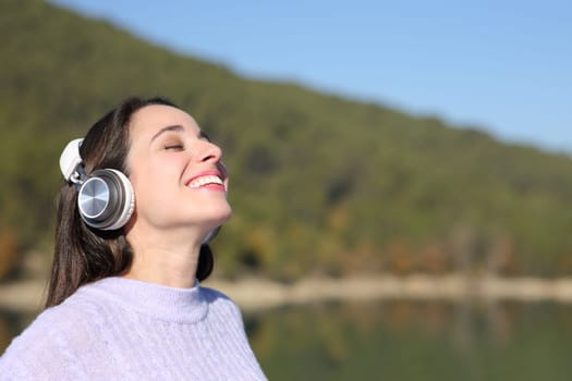 Happy woman meditating with wireless headphones in a beautiful lake