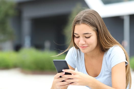 Teenage female checking smart phone sitting alone in the street