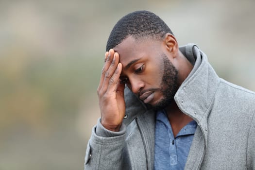 Worried man with black skin complaining in winter walking in a park