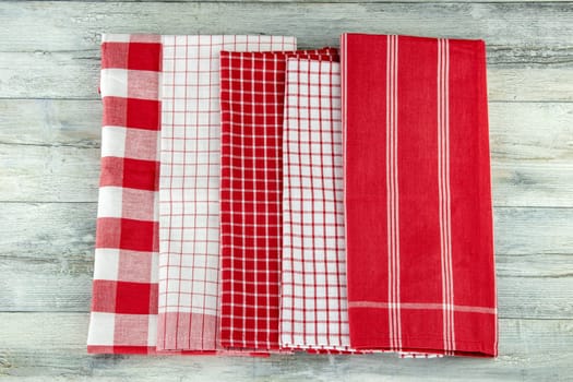 Top view of a set of empty red and white checkered and striped kitchen cloth, textile, tablecloth or napkin on rustic bright wooden table. Template for product display montage.