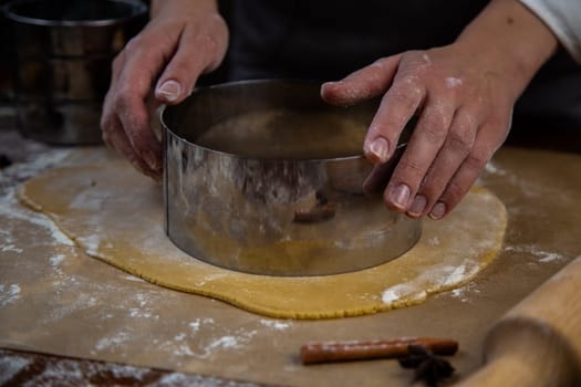 The rolled out layer of dough lies on baking paper, a cake cake is cut out of it with a metal cutter. High quality photo