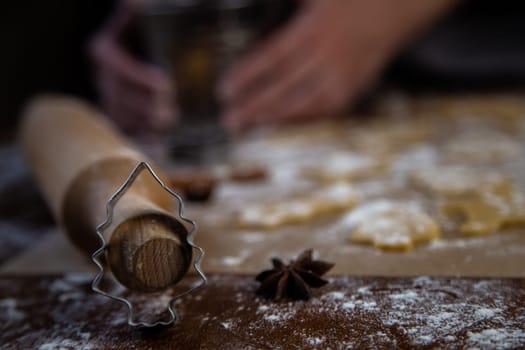 A Christmas tree-shaped mold stands leaning on a rolling pin against a background of cookies, parchment and flour cut out of dough. Photos in dark colors. High quality photo