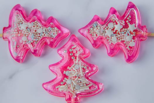 Three pink Christmas trees lollipops on a wooden leg with powder inside lie on a light marble background. High quality photo