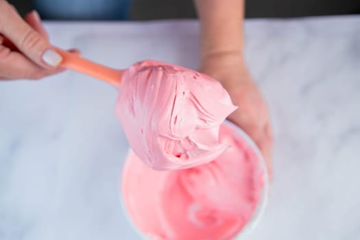 Pink confectionary meringue marengo is mixed in a white bowl on a white marble background by the hands of a pastry chef. High quality photo