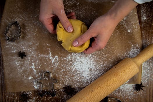 In the foreground is a table with baking parchment lying on it, on which there is dough that the cook's hands are crumpling, a rolling pin, baking molds and flour are scattered around. High quality photo