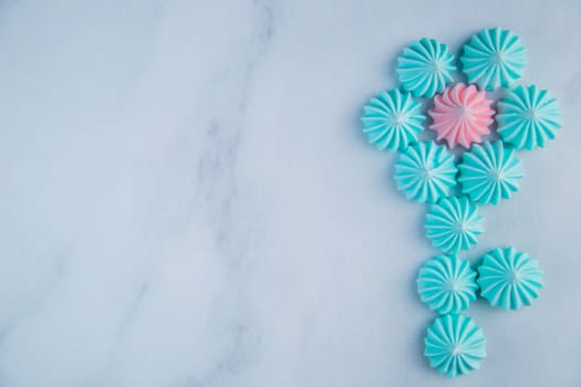 A flower with turquoise petals and a pink core with a stem made of meringue bizet lie on a light marble background with a place for text. High quality photo