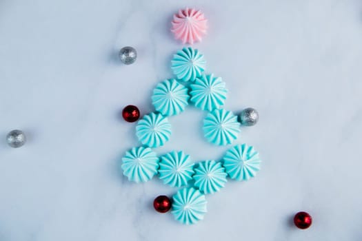 A Christmas tree made of turquoise meringue with a pink star at the end lies on a light marble background with a place for text. High quality photo