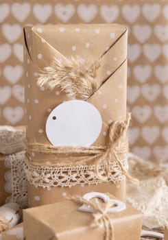 Valentines kraft paper wrapped present with round gift tag, hearts and pampas grass close up. Spring scene with blank label. Rustic, cottage chic or bohemian mockup, copy space