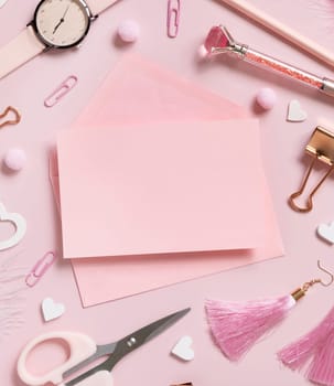 Pink paper card with envelope, school accessories and hearts on pastel pink top view, blank card mockup. Girly workplace. Back to school and valentines day concepts