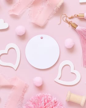 Blank round gift tag, hearts, flowers, silk ribbons and tassel earrings on pink top view. Romantic scene with blank label mockup flat lay. Valentines day, wedding and girly concept.