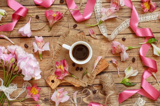 Coffee cup, ribbons, petals and pink flowers on wooden table top view. Romantic breakfast, Spring and valentines day flat lay