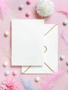 Blank card and envelope near pastel flowers, pom-poms and feathers near ring in a gift box on pink top view. Romantic scene with wedding stationery, place for text flat lay. Valentines, Spring or girlish concept