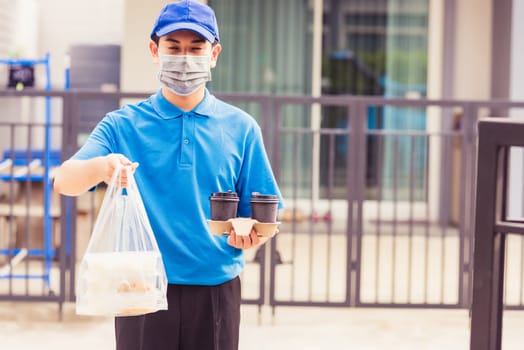 Asian young delivery man in blue uniform wearing face mask making grocery service giving rice food boxes plastic bags and coffee at front house under pandemic coronavirus, Back to new normal concept