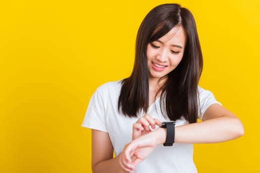 Portrait Asian of a happy beautiful young woman smiling looking and pointing finger her smart wristwatch studio shot isolated on yellow background