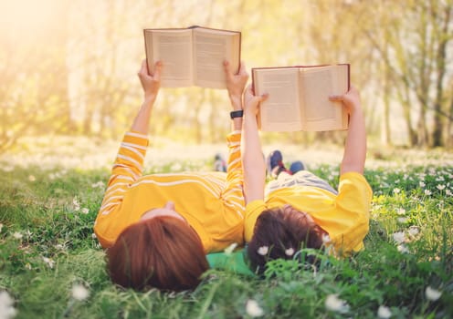 Mother and her son lying down on the beautiful spring field in the sunny park. Concept of the interesting of literature and family leisure.