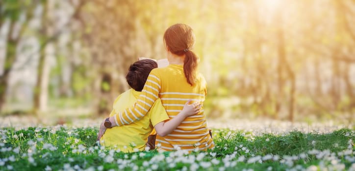Mother and her son sitting n on the beautiful spring field in the sunny park. Concept of the interesting of literature and family leisure.