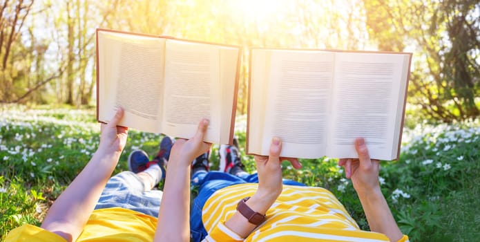Mother and her son lying down on the beautiful spring field in the sunny park. Concept of the interesting of literature and family leisure.