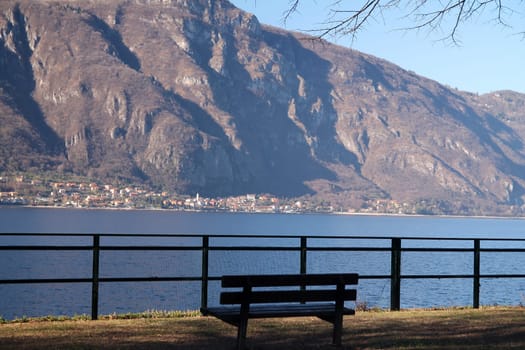 Close up of a brown bench looking at the lake and Alps on the shore of Lake Como in Italy