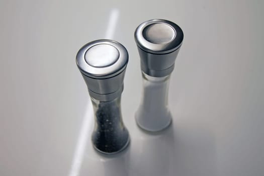 Salt and pepper glass and iron grinders on a white desk redy to be used