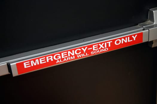 Emergency exit only alarm wall push handle on a black security door in an industrial space