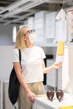 New normal during covid epidemic. Caucasian woman shopping at retail furniture and home accessories store wearing protective medical face mask to prevent spreading of corona virus.