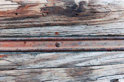 Full-frame view of a rusty metal rail in weathered wood.